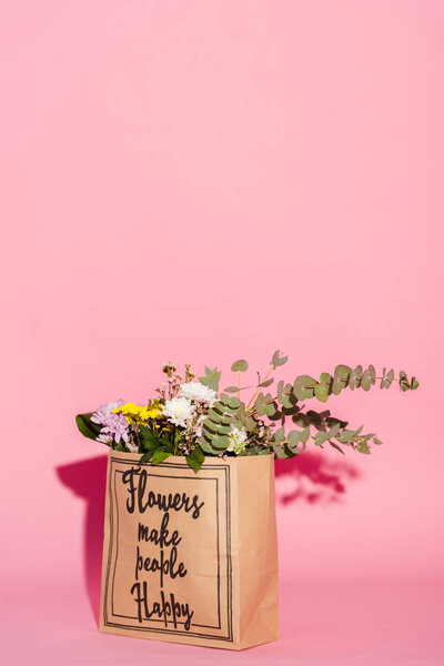 bouquet of flowers and eucalyptus leaves in paper bag with flowers make people happy lettering on pink