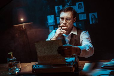 Karanlık ofiste daktilo kullanırken gözlüklü Dedektif puro sigara