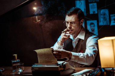 Karanlık ofiste daktilo kullanırken gözlüklü Dedektif puro sigara