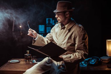 Dedektif, hendek ceket ve şapka tutan dosyam ve fotoğrafa bakıyor