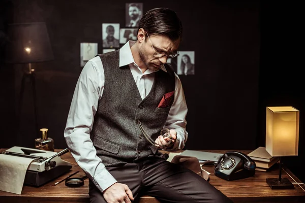 Concentrated Detective Glasses Sitting Wooden Table Looking Pocket Watch Office — Stock Photo, Image