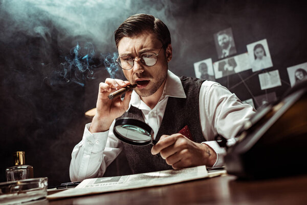 Detective in glasses smoking cigar and reading newspaper with magnifier in office