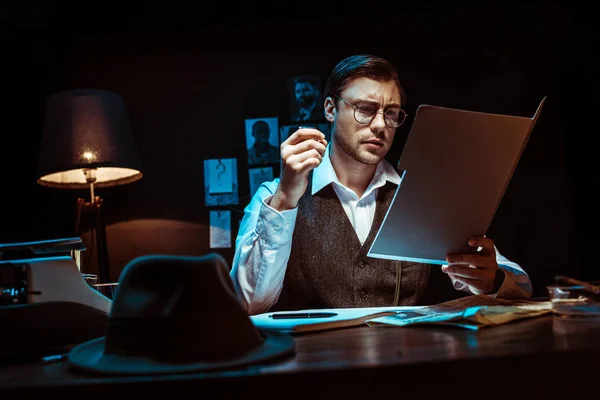 集中的侦探在眼镜阅读档案在黑暗的办公室 — 图库照片