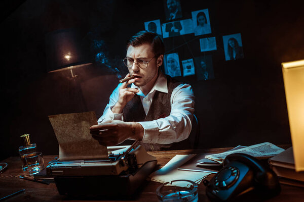 Detective in glasses smoking cigar while using typewriter in dark office