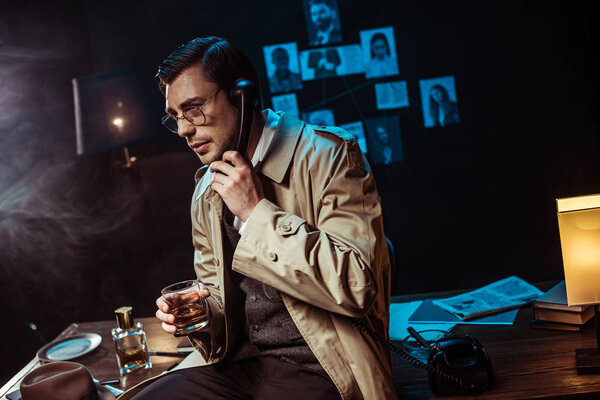 Detective in glasses talking on telephone and holding glass of cognac