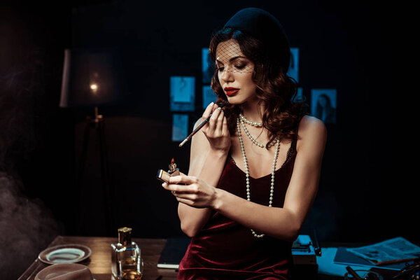 Красивая женщина с мундштук зажигает сигарету с зажигалкой в темном офисе
