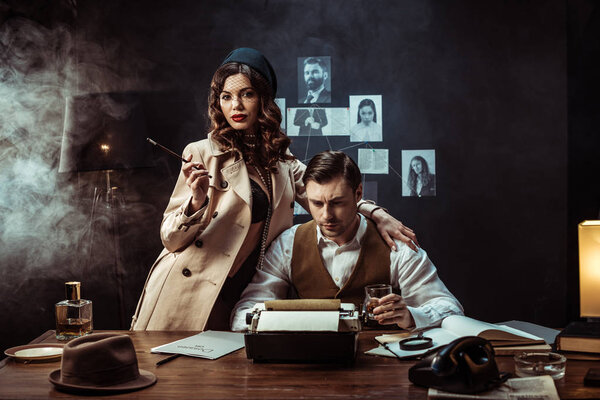 Женщина с рупором стоит рядом с детективом в темном кабинете
