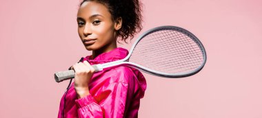 panoramic shot of beautiful african american sportswoman holding tennis racket isolated on pink  clipart