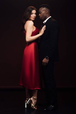 beautiful woman in fashionable red dress posing with african american man in suit isolated on black clipart