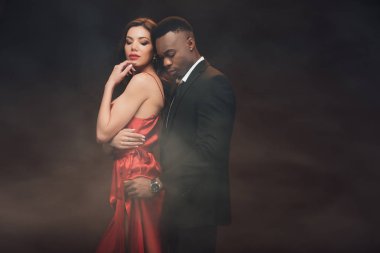 african american man embracing beautiful woman in red dress on dark with smoke clipart