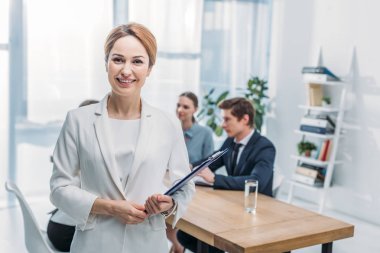 selective focus of cheerful recruiter standing with clipboard near coworkers  clipart