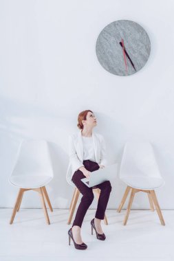 güzel çalışan dizüstü bilgisayar ile sandalyeye oturan ve saat bakıyor