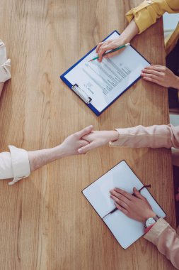 top view of woman shaking hands with recruiter near coworker with clipboard and pencil  clipart