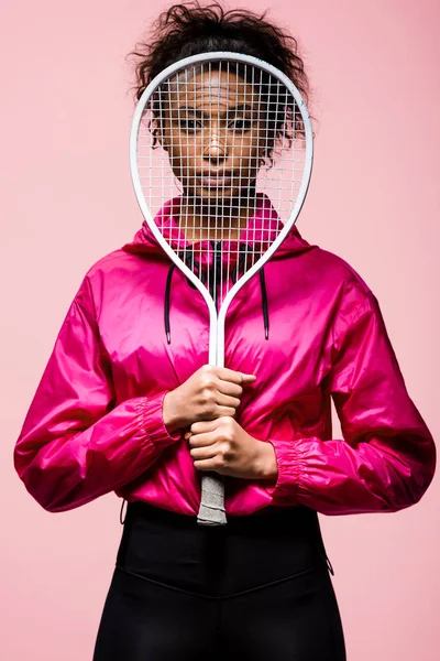 非洲裔美国女运动员看着相机 同时覆盖与网球拍隔离粉红色 — 图库照片
