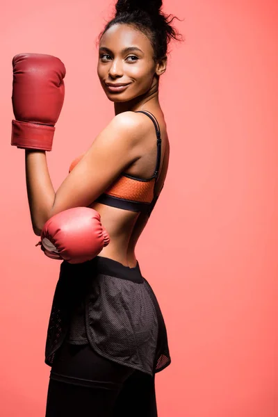 attractive african american sportswoman in boxing gloves posing isolated on coral with copy space
