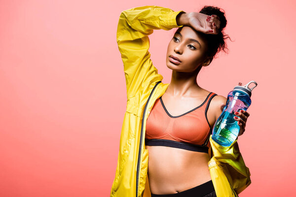 beautiful african american sportswoman with sport bottle posing isolated on coral with copy space