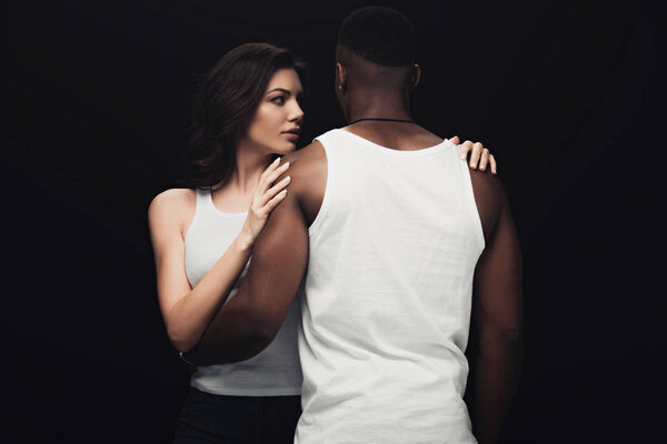 beautiful seductive woman embracing african american man isolated on black