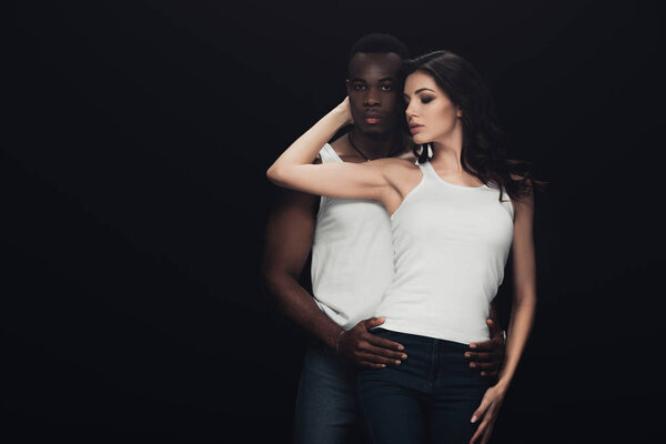 african american man embracing beautiful woman and looking at camera isolated on black with copy space