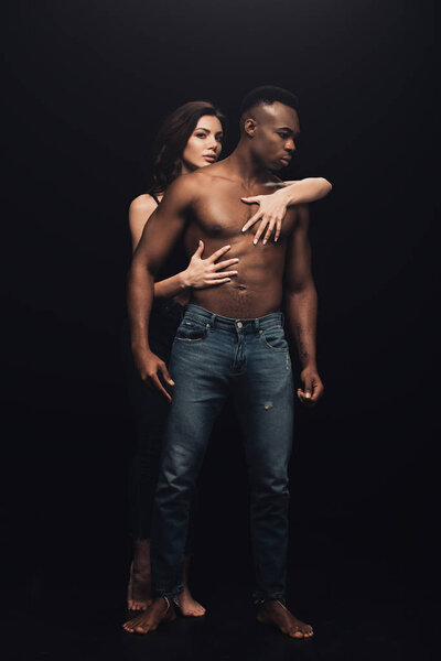 beautiful sexy woman hugging shirtless african american man in denim isolated on black