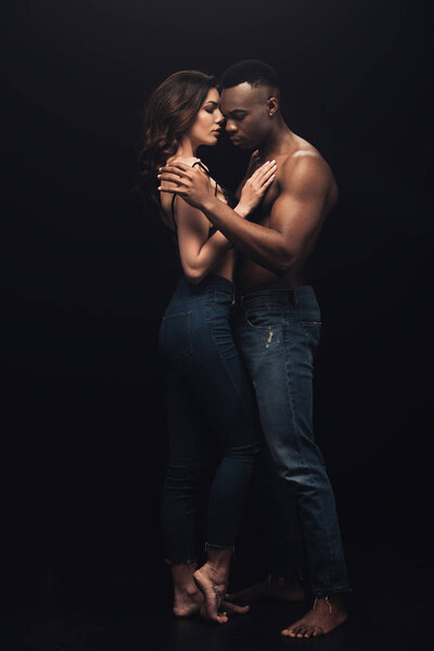 beautiful sexy interracial couple in denim embracing isolated on black