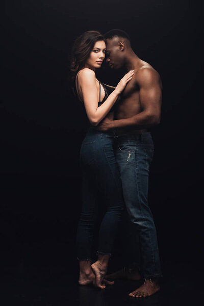 beautiful sexy interracial couple in denim embracing isolated on black