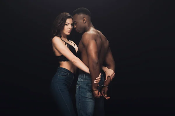 上半身裸アフリカ系アメリカ人男性を抱きしめた美しいセクシーな女性コピースペースで黒に分離された手錠 — ストック写真