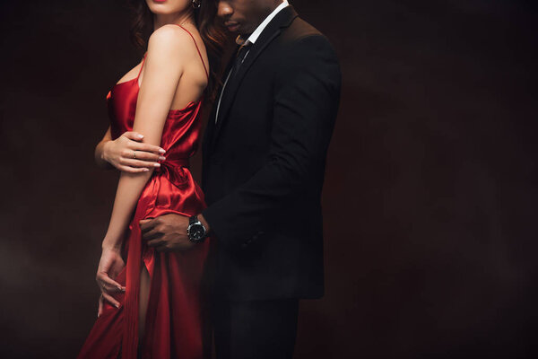 cropped view of african american man embracing woman in red dress isolated on black with copy space