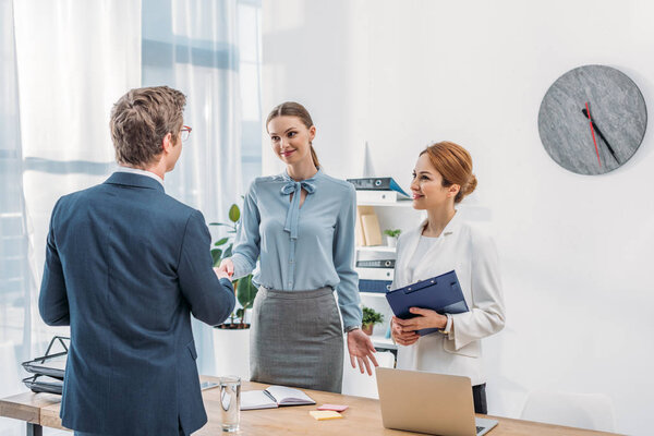 back view of man shaking hands with happy recruiter near colleague in office