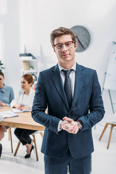 selective focus of recruiter in glasses standing with clenched hands near coworkers 