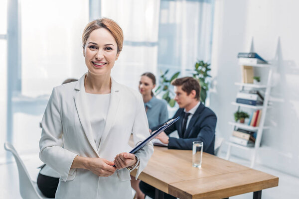 selective focus of cheerful recruiter standing with clipboard near coworkers 