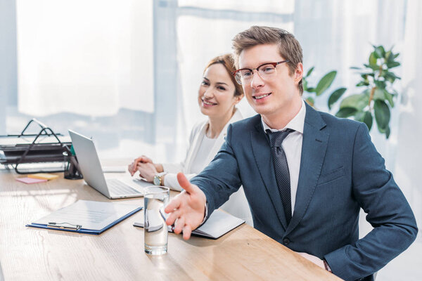 handsome recruiter in glasses gesturing near cheerful coworker 
