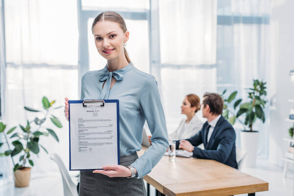 selective focus of happy recruiter holding clipboard with resume cv lettering near coworkers 