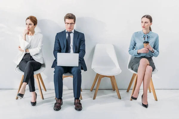 worried woman sitting with crossed legs and crossed arms near man using laptop