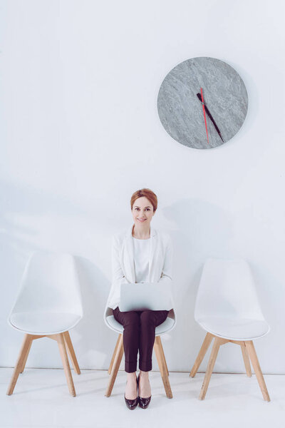 cheerful employee sitting on chair with laptop while waiting job interview 