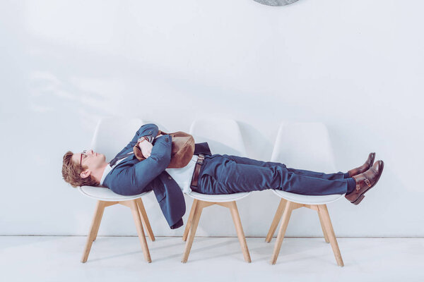 handsome employee in glasses lying on chairs while waiting job interview 