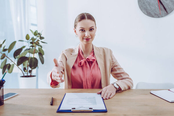 cheerful and attractive recruiter gesturing near clipboard in office 