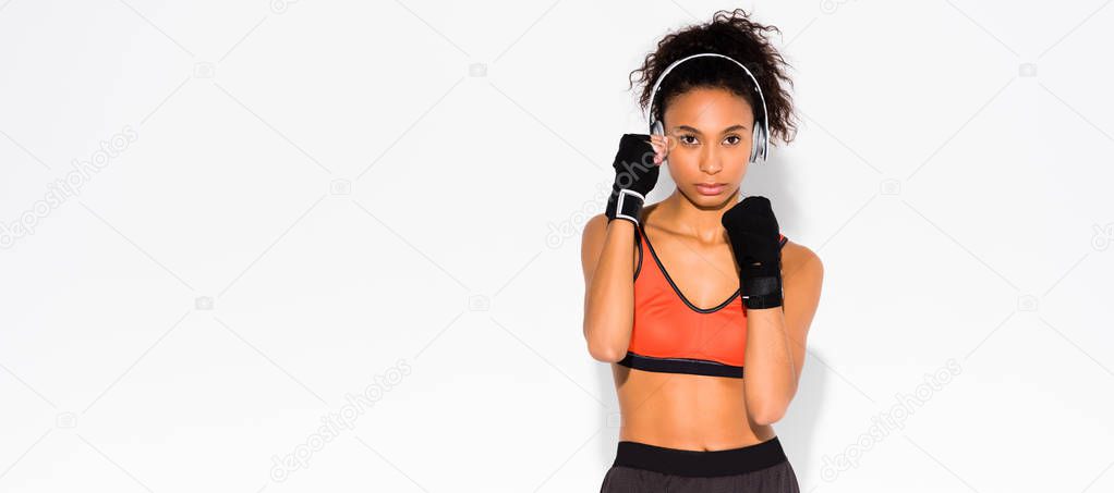 panoramic shot of athletic african american sportswoman in sport gloves looking at camera on white