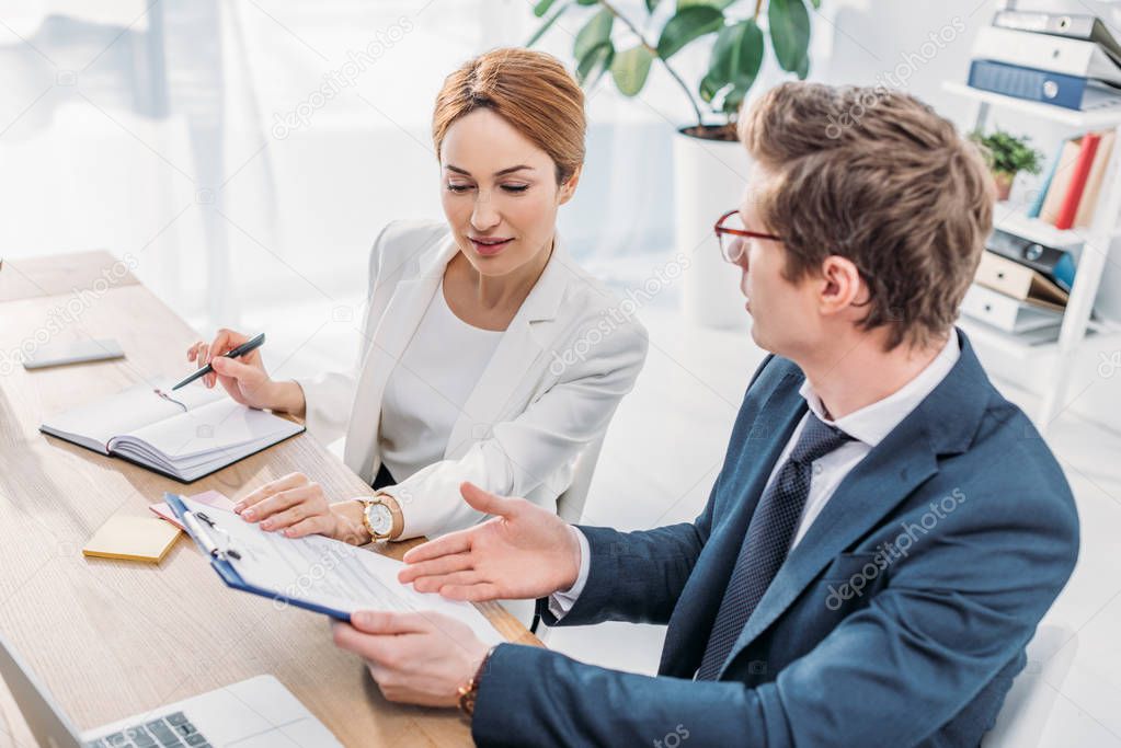 overhead view of attractive hr looking at clipboard with document near coworker in glasses 