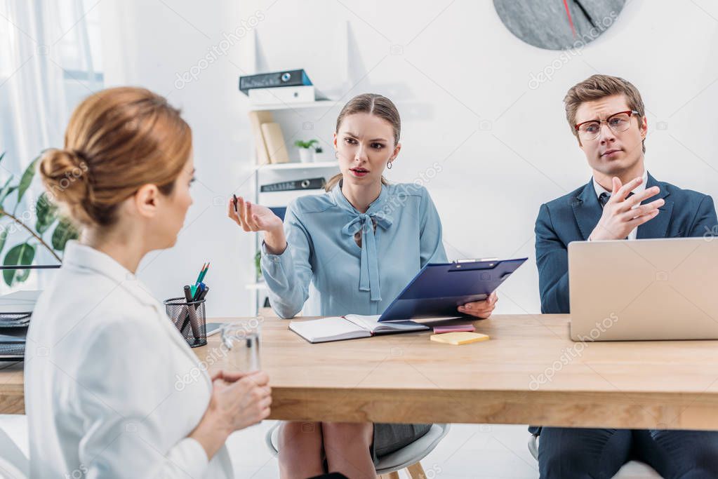 attractive recruiter talking with woman and holding clipboard near coworker in glasses 