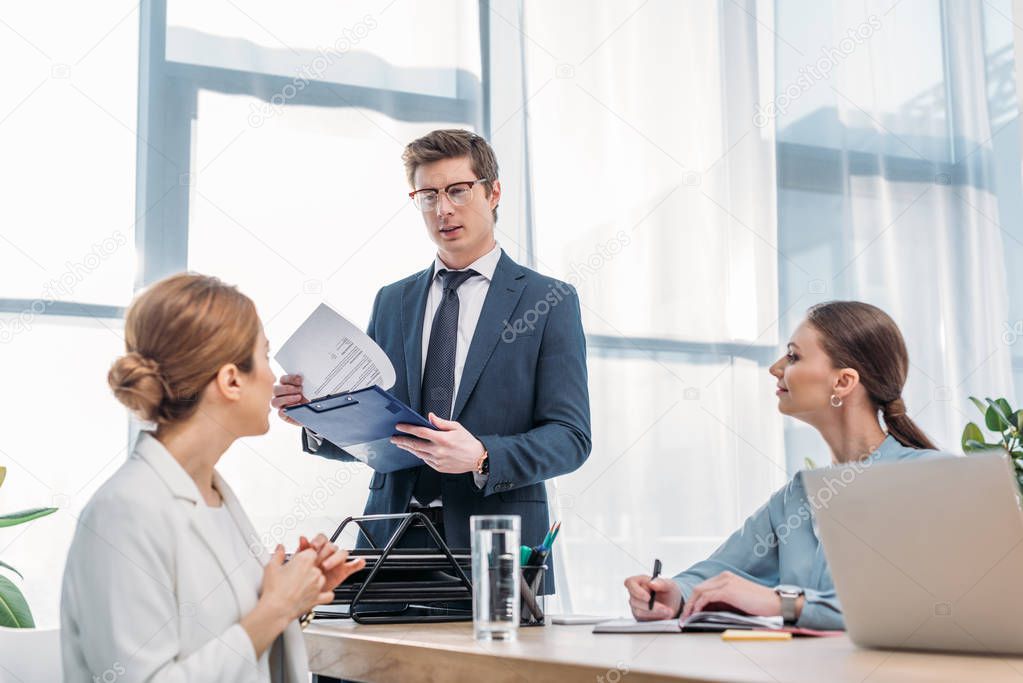 handsome recruiter holding clipboard and looking at woman in job interview 