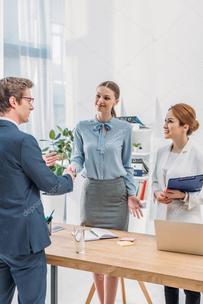 cheerful employee shaking hands with happy recruiter near colleague in office