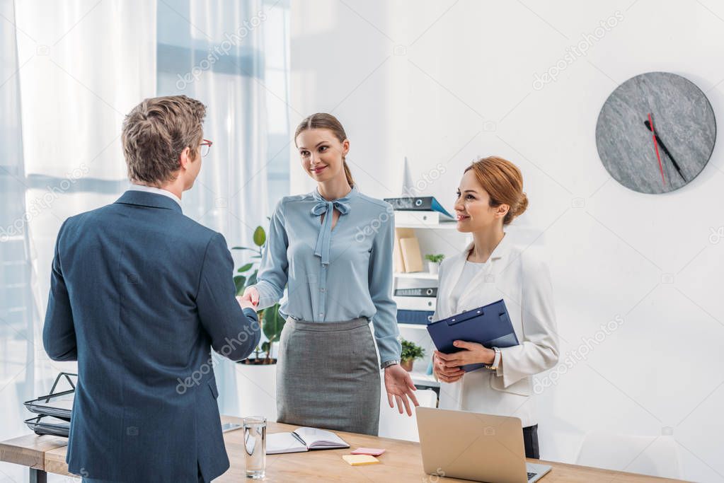 back view of man shaking hands with happy recruiter near colleague in office