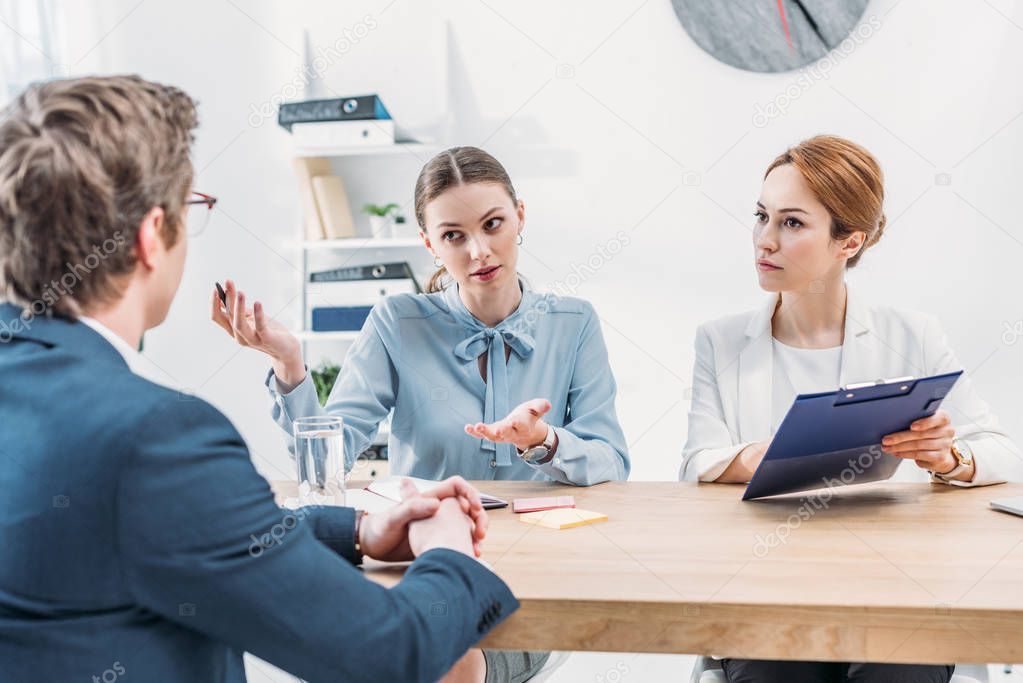 attractive recruiters talking with man sitting with clenched hands during job interview 
