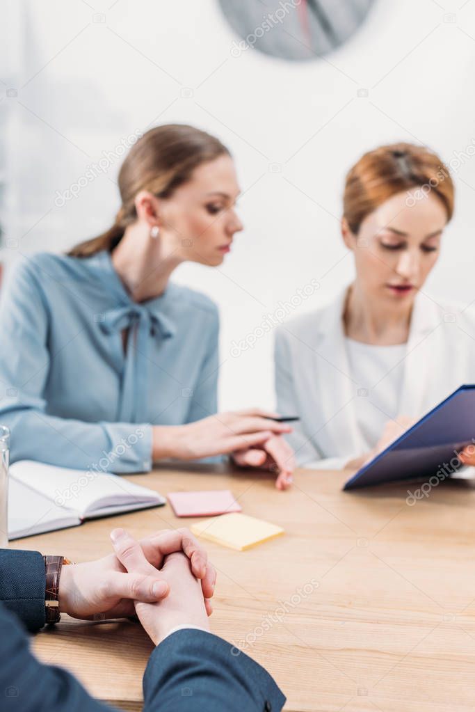 selective focus of man sitting with clenched hands near attractive recruiters