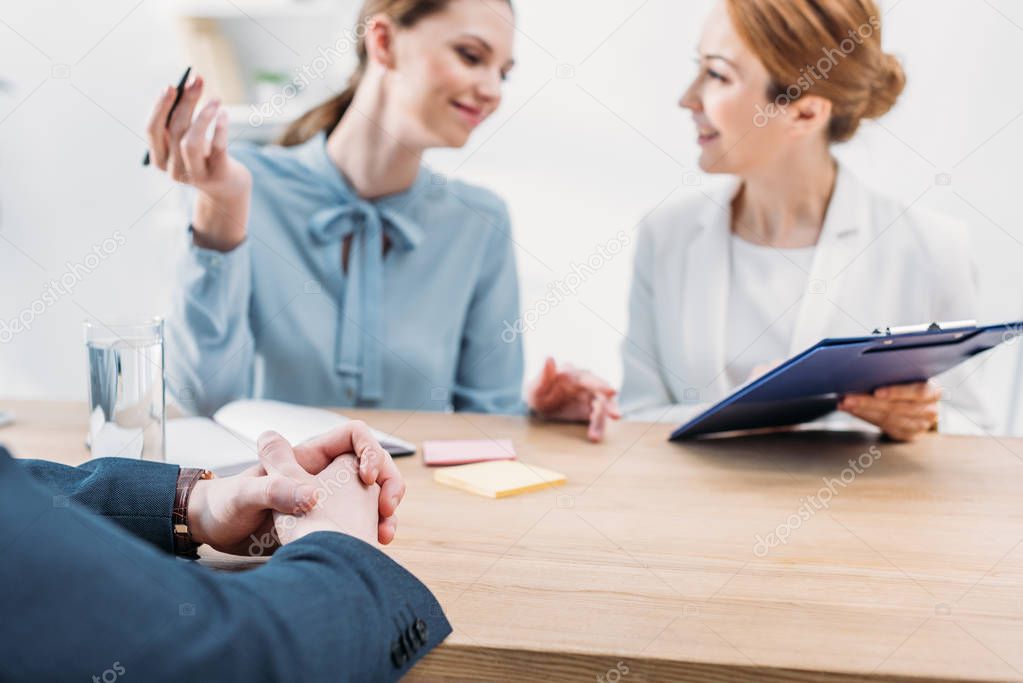 selective focus of man sitting with clenched hands near happy recruiters