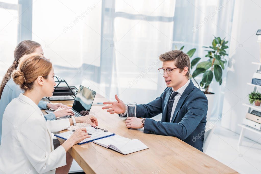 handsome employee in glasses talking and gesturing on job interview 