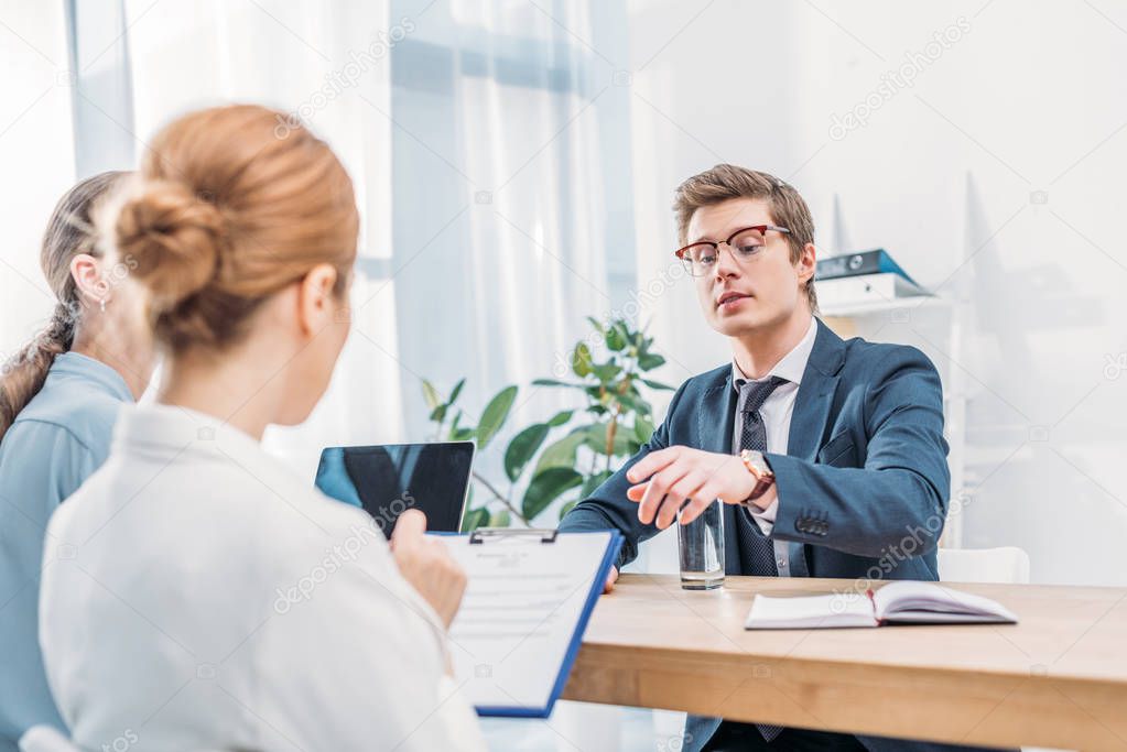 selective focus of man in glasses pointing with finger at recruiter with clipboard 