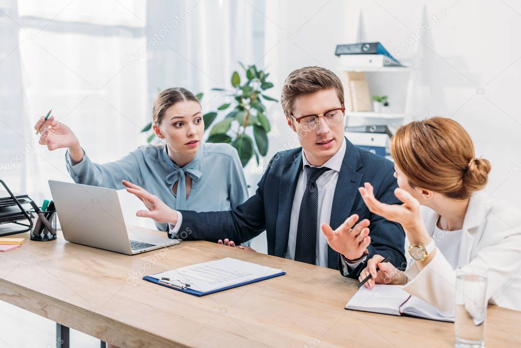 handsome man in glasses gesturing while talking with attractive coworkers 