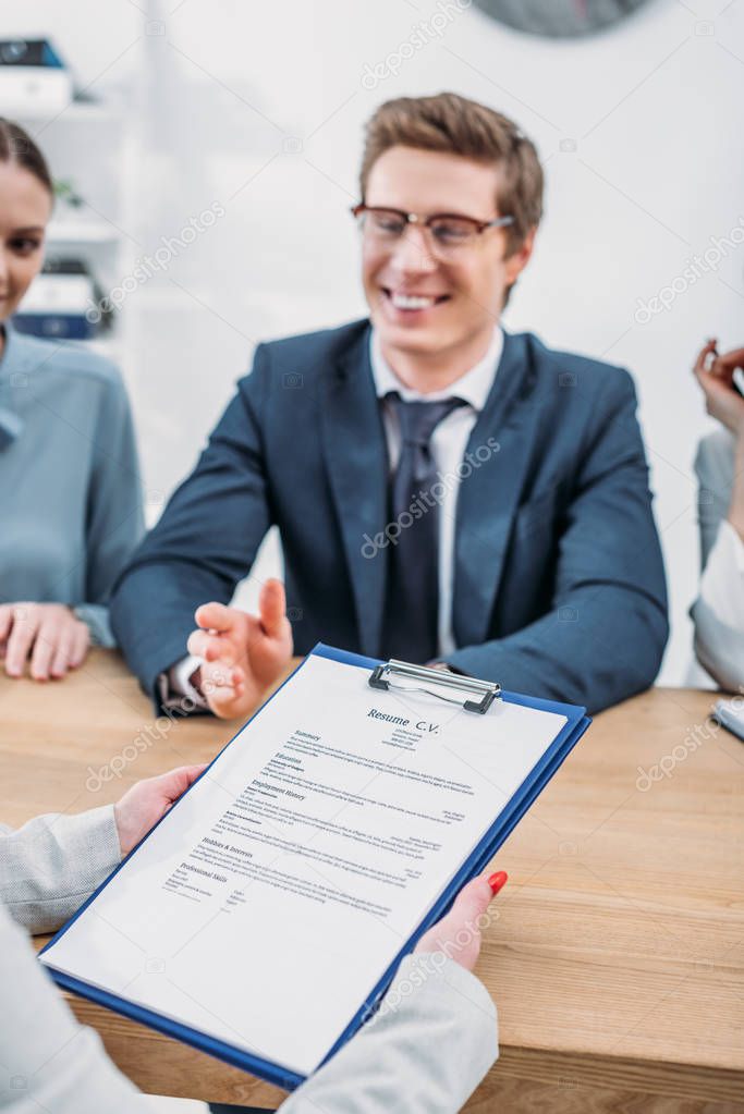 cropped view of woman holding clipboard with resume cv lettering near recruiters 