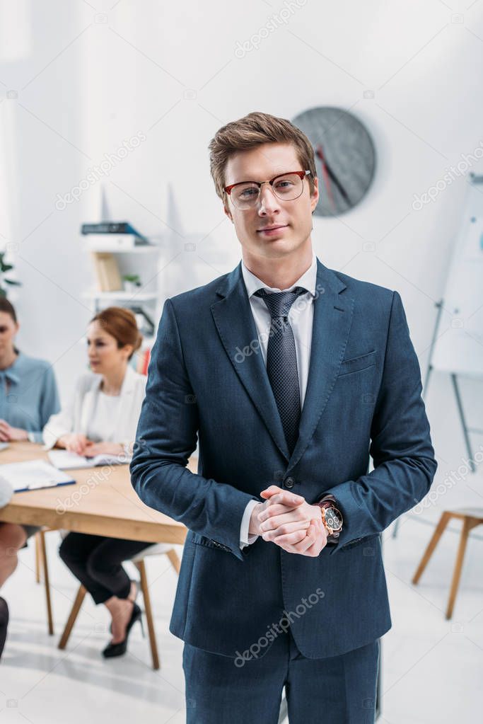 selective focus of recruiter in glasses standing with clenched hands near coworkers 